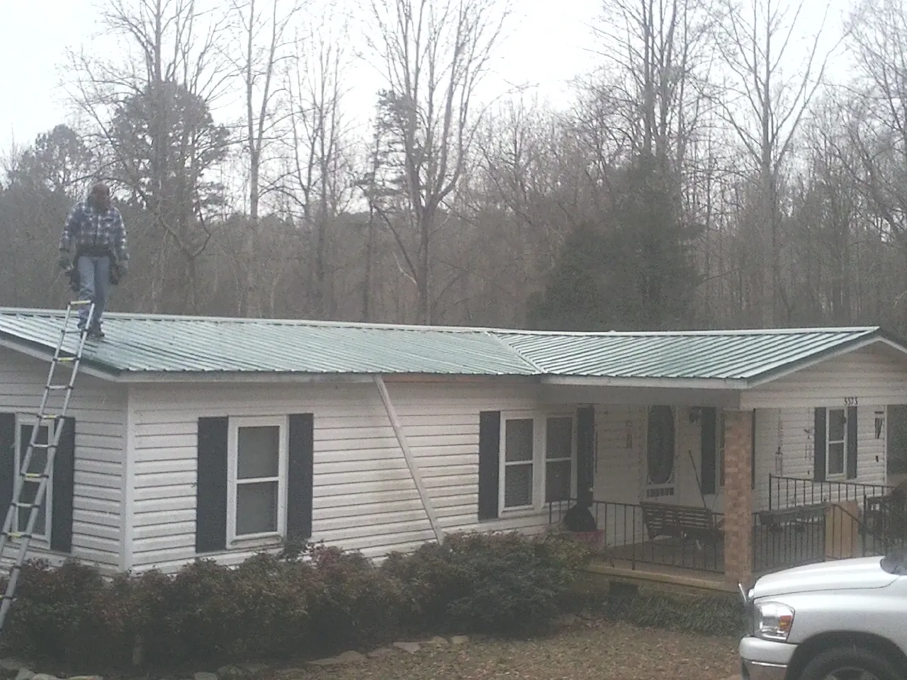 Worker on a ladder beside a new green metal roof on a ranch home in Waycross
