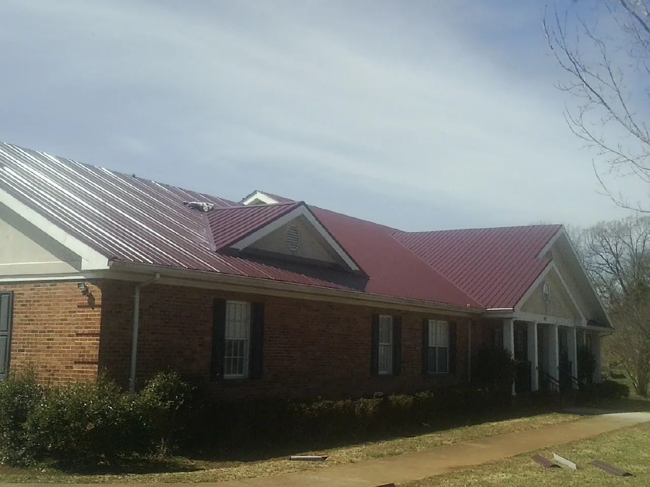 Red metal roof with gabled entries on a long brick building, from a Hail Damage Roof Repair job in Waycross