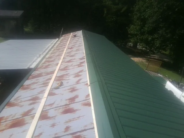 Old rusted panels beside newly installed green metal roofing — Wind Damage Roof Repair by Roofing Brothers in Waycross