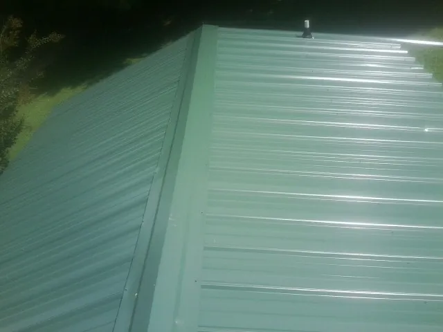 New green metal panels meeting at the ridge of a roof — Flat Roof Repair work by our crew in Waycross
