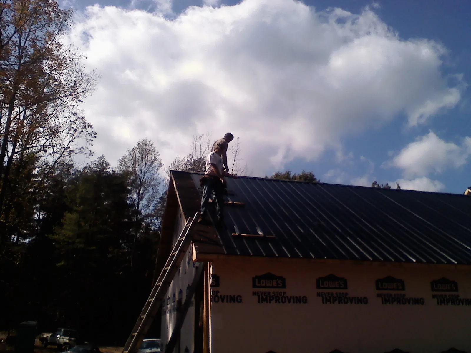 Roofer fastening dark metal panels high against a cloudy sky, from a Roof Inspection job in Waycross