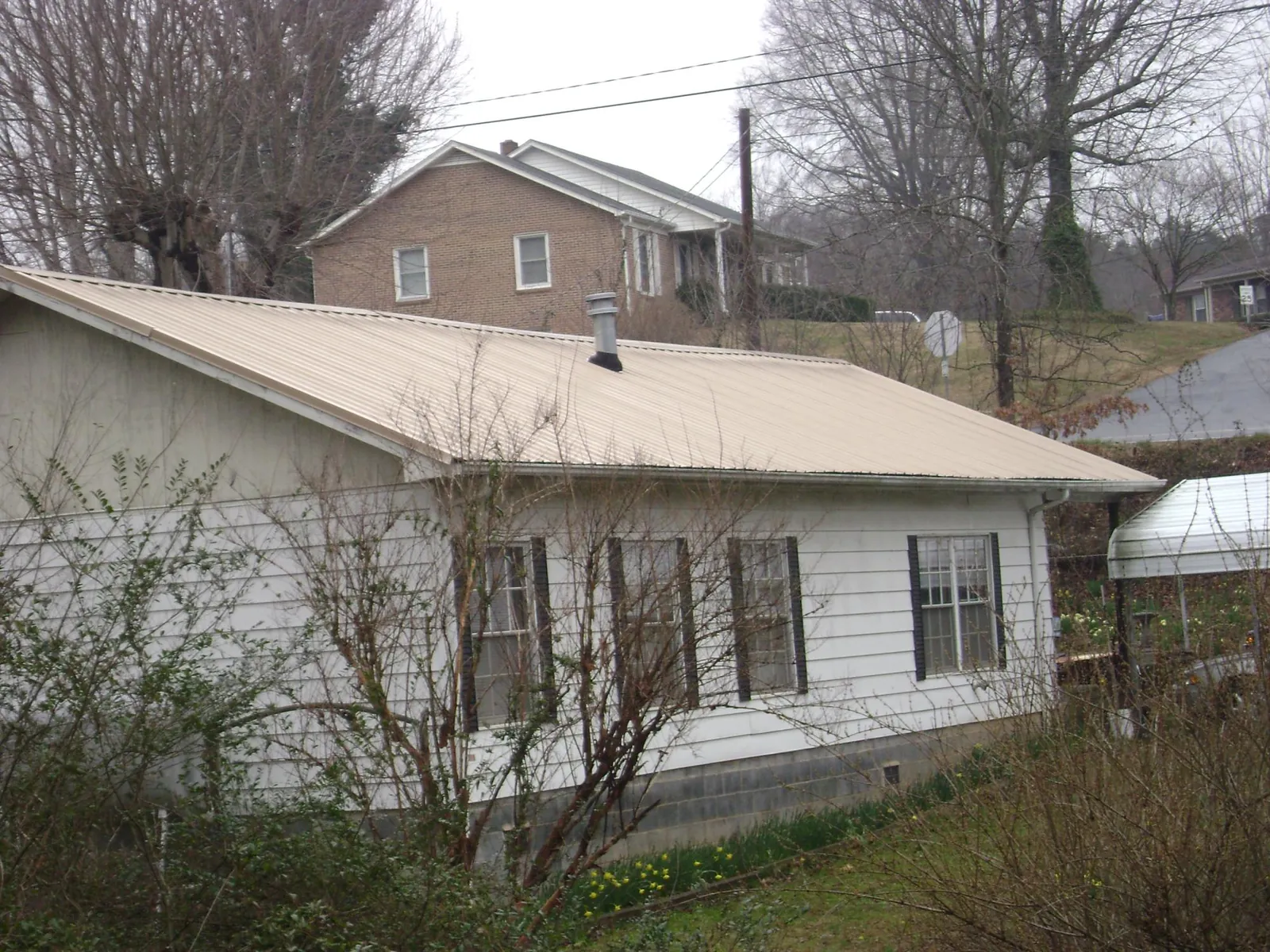 Tan metal roof on a white sided house set into a hillside — Commercial Roofing by Roofing Brothers in Waycross