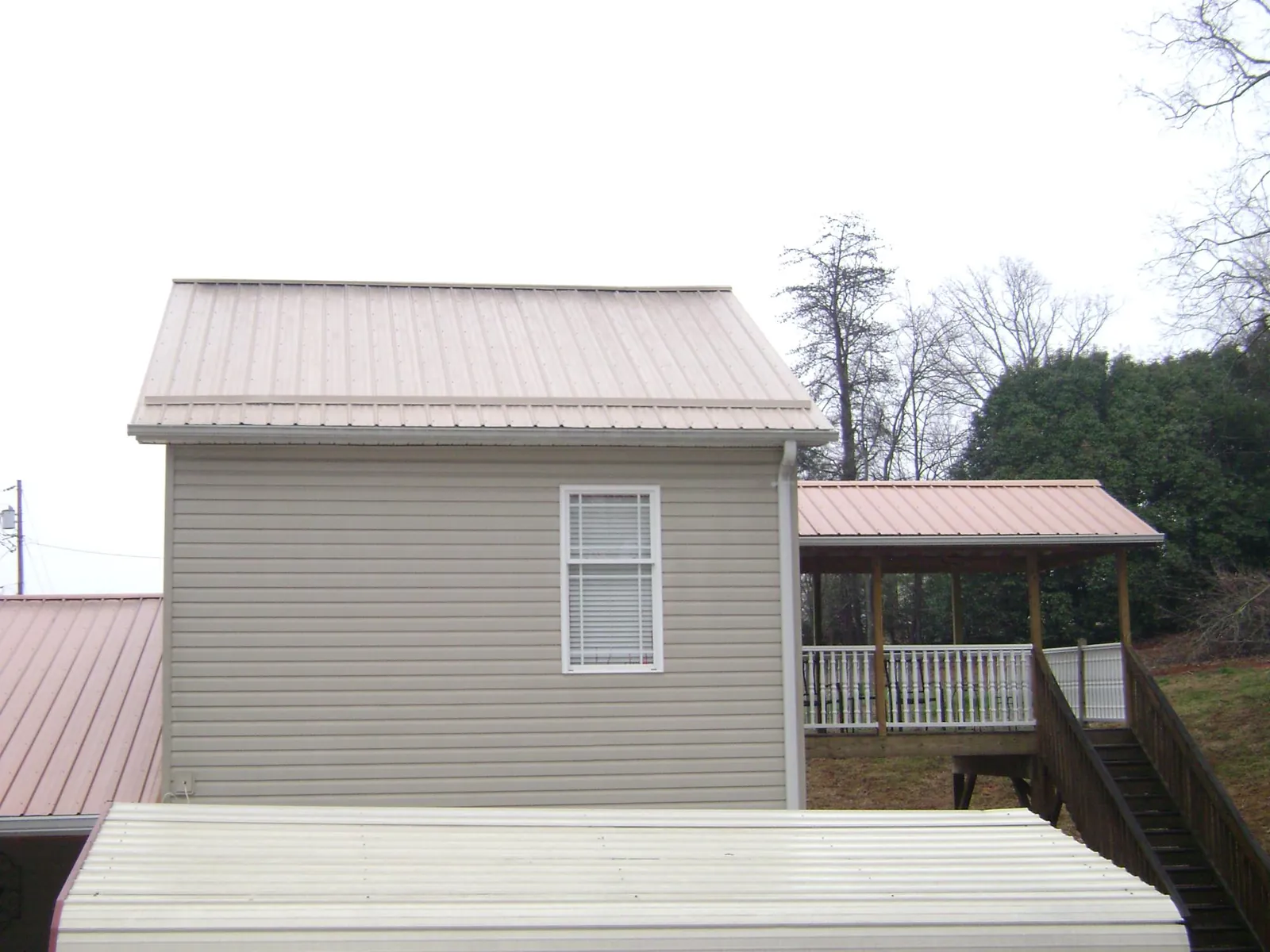 Tan metal roofs on a two story addition and attached porch, from a Roof Replacement job in Waycross